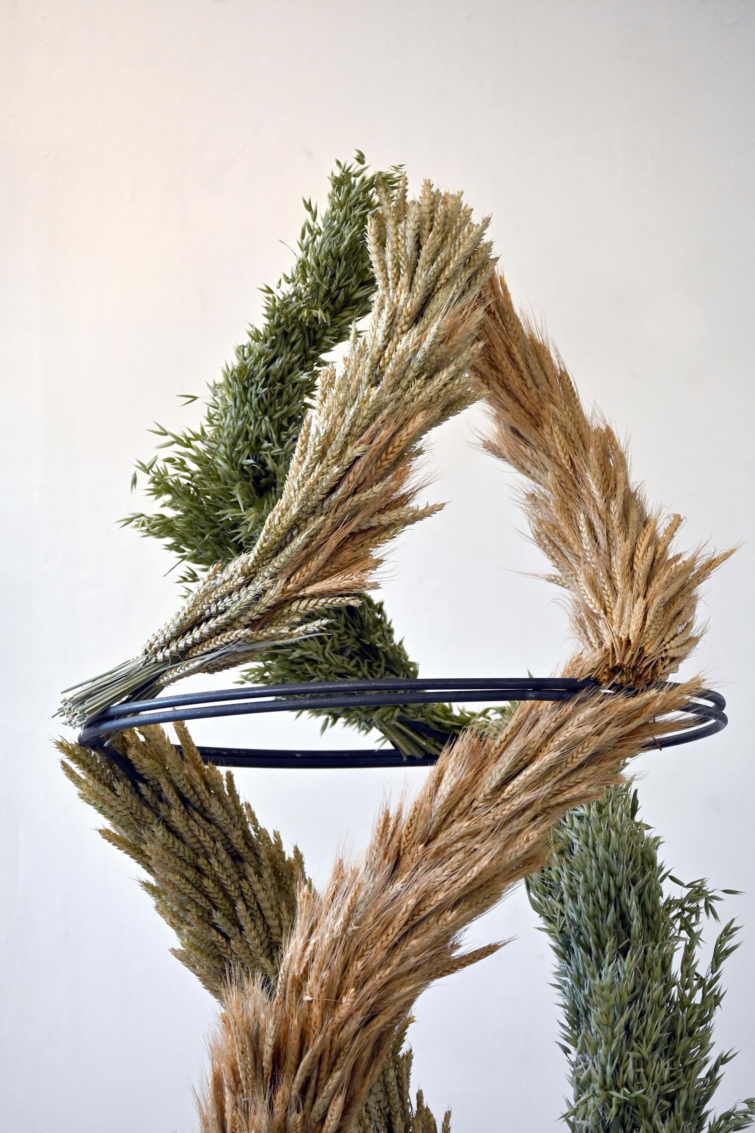 Close up of a sculpture made from three garlands of wheat (brown, yellow, and green) swirling around each other and joining at the top.