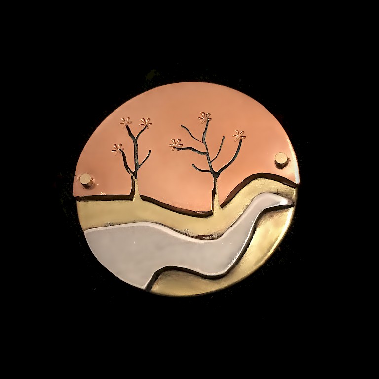 Brooch by Bramble and Bert, depicting two trees and a stream, in copper, brass, and silver.