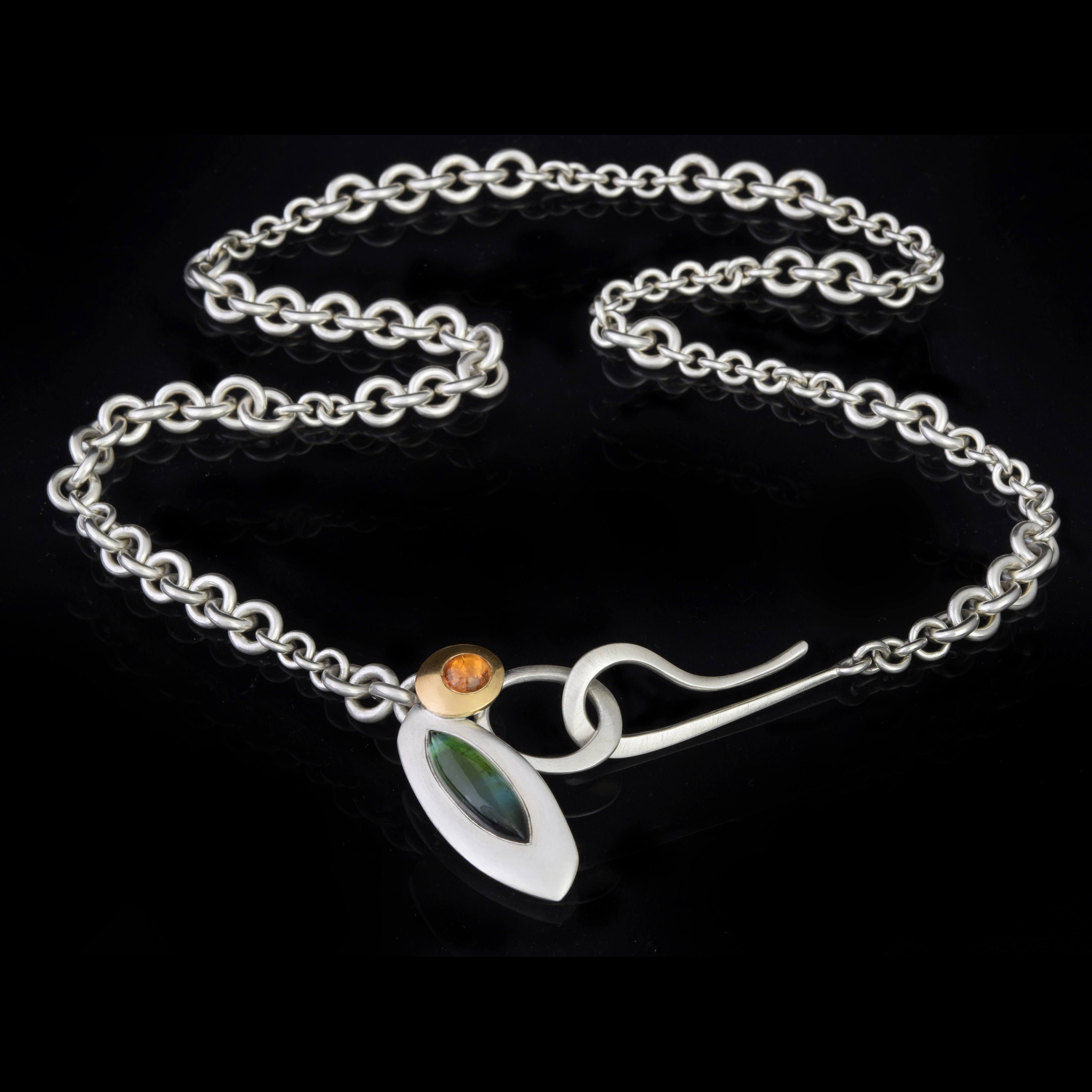 Necklace by Emily Thatcher, chain with varied thickness and a large hook fastener, with silver and gold pendants featuring green and orange gemstones.