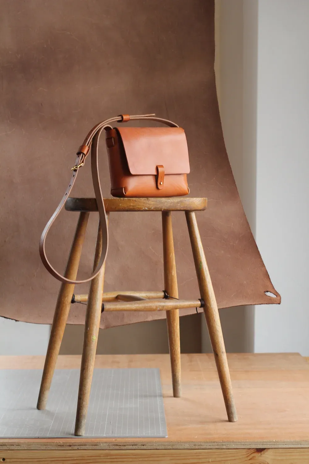 Handbag by Jonathan Hyde in tan leather, displayed on a wooden stool.