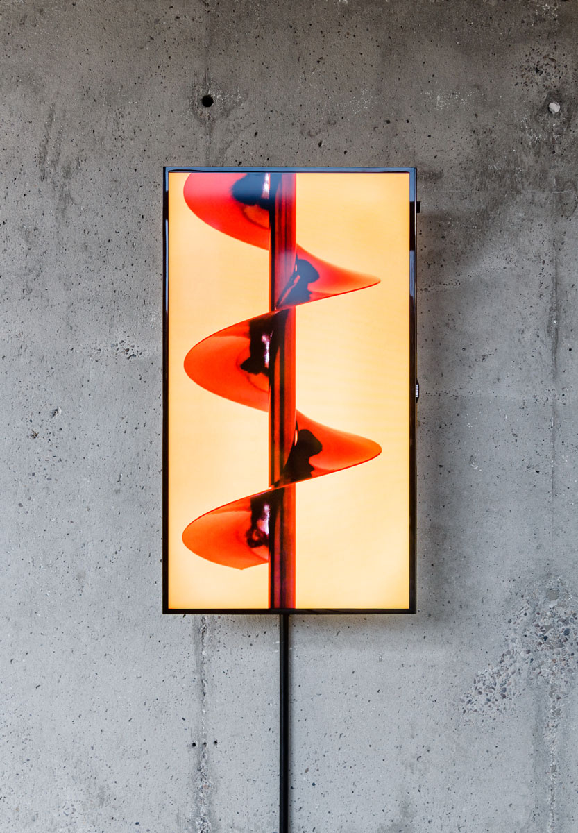 Video work by Joseph Cutts, portrait-oriented like a smartphone, showing a closeup of red large drillbit or mixing tool rotates against an orange background.