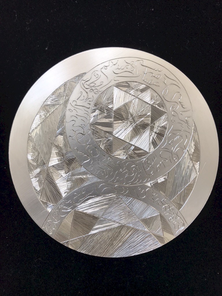 Artwork by Morvarid Alavifard, a silver disc intricately engraved with Farsi calligraphy and fine markmarking. Concentric circle design with geometric stars of David.