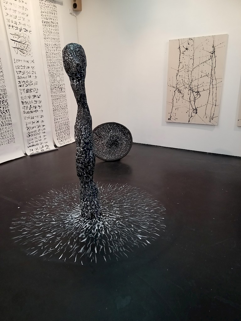 Installation by Norman Anderson featuring a tall worm-like sculpture, long scrolls of calligraph-like writing, and a black painting.