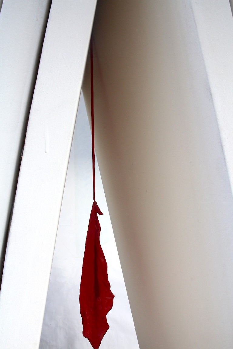 Artwork by Robert Clark, a scrap of red material hangs from the corner of a white room.