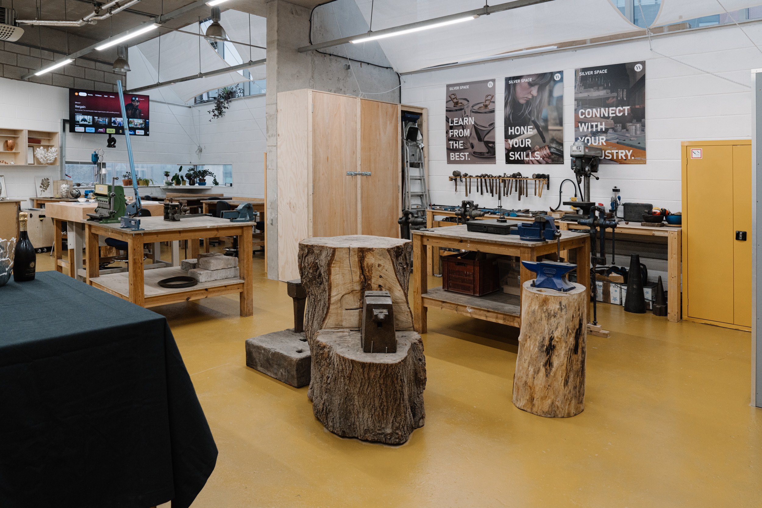 View of Yorkshire Artspace silversmithing studio with anvils, workbenches, and tools hung on the walls, signs reading: "Learn from the best, hone your skills, connect with your industry".